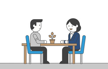 Two people sitting at a table with a small plant, engaged in conversation.