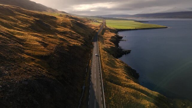 Car driving at sunset along a cliffside road in the fjords, with the ocean beside it. Scenic landscape with warm colors and dramatic coastal views.