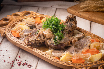 Traditional Kazakh beshbarmak arranged on a festive carved platter with meat vegetables and herbs