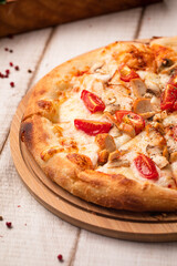 Hot chicken pizza topped with cherry tomatoes, cheese and spices on a wooden board