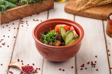 Stewed meat with potatoes and vegetables served in a rustic clay pot with fresh cucumber and tomato slices