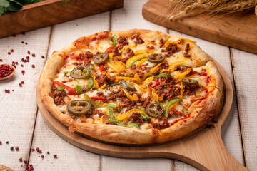Mexican style pizza with jalapeno slices, ground meat, cheese and vegetables on a wooden board