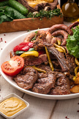Assorted grilled meats with vegetables, herbs and fried potatoes served on a large round plate