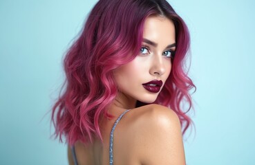 Young woman with pink and purple hair posing. Female model with colorful hair, classic makeup. Adult girl turns back and looks at camera on blue background. Attractive person with wavy hairstyle.