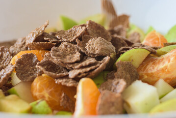 Healthy breakfast with fruit salad and muesli, closeup photo. Bran flakes on top of chopped fruits in bowl, healthy breakfast concept