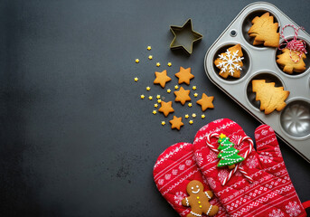 On a dark table, Christmas cookies, gingerbread men, snowmen, oven mitts, and a cookie cutter set. Winter holiday baking concept, top view.