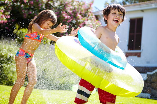 Floatie, kids or playing with sprinkler in garden for summer fun, sensory stimulation and bonding. Happy family, children or adventure on lawn with water irrigation, inflatable tube or funny activity