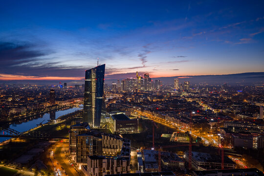 Aerial view of the European Central Bank skyscraper piercing the twilight sky over the Main River, a beacon amidst Frankfurt's illuminated cityscape, Frankfurt am Main, Hessen, Germany.