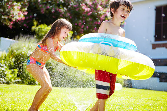 Inflatable, children or playing with sprinkler in garden for summer activity, fun bonding and laughing. Happy family, kids and floatie on lawn with water irrigation, sensory stimulation and adventure
