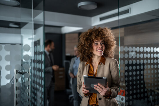 Confident businesswoman smiling and holding tablet in office