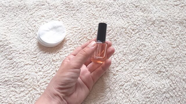 Woman holding and displaying a nail care oil bottle in a close-up overhead. shot woman&rsquo;s hand rotating and showing a nail care oil bottle in a manicure salon or bathroom interior