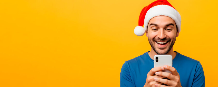 Happy man in Santa hat looking with smile at mobile phone in Christmas holiday. Communication on smartphone in holiday in studio on orange background, banner