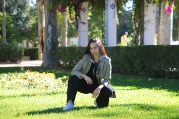 Young, attractive Spanish woman with dark hair crouching with one leg stretched out on the grass in...
