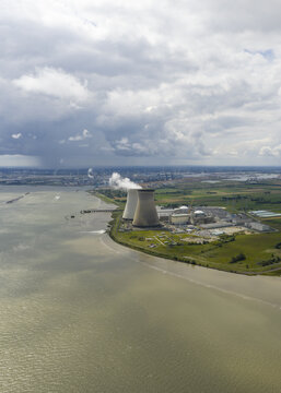 Aerial view of the Doel Nuclear Power Plant standing tall against the cloudy sky, its cooling towers emitting plumes of vapor above the Scheldt river, Beveren-Kruibeke-Zwijndrecht, Flanders, Belgium.