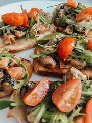 Toasted Bruschetta with Mussels, Cherry Tomatoes, and Arugula. A delicious close-up of multiple pieces of toasted bruschetta, generously topped with mussels, halved cherry tomatoes, and fresh arugula.