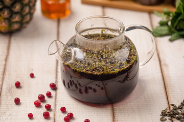 Warm herbal tea infusion brewed with leaves and berries served in a glass teapot on rustic wooden table
