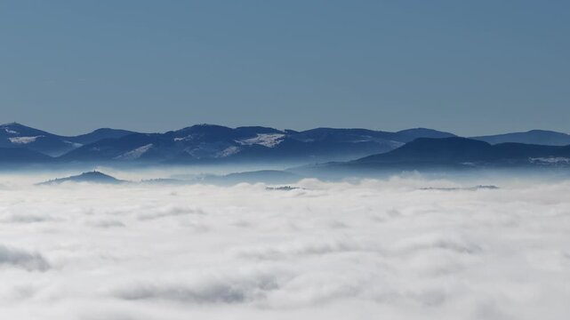 Aerial view of a sea of clouds with the tips of dark mountains poking through, with snow-capped peaks in the distance, Orschwiller, Grand Est, France.