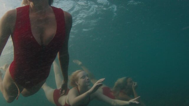 Three young sensual women in red swim suits dive under the breaking ocean wave