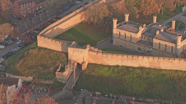 Roman fortress Lincoln Castle's historic walls encapsulating the prison and grounds, creating a protective barrier against the surrounding urban landscape of Lincoln, England, in warm sunset light