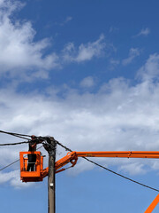unrecognisable man electrician worker standing in an orange bucket crane repairing high voltage power line electrical cable outdoors