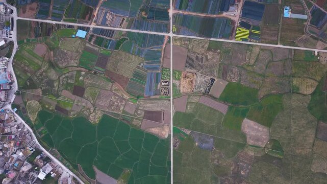 Top-down drone shot of colorful patchwork farmland in Huishui, Guizhou, showing fields, greenhouses, rural roads and agricultural patterns across a vibrant countryside landscape. China.