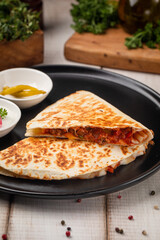 Chicken quesadilla served on a black plate with sauces and fresh herbs