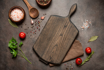 Culinary background with empty wooden cutting board, wooden spoon and spices, dark grunge background, top view, flat lay, copy space.