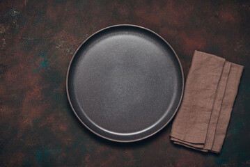 Empty brown plate and linen napkin on dark rusty background, top view, flat lay, copy space