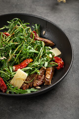 Flavorful arugula salad mixed with tender beef slices sundried tomatoes parmesan and herbs on plate