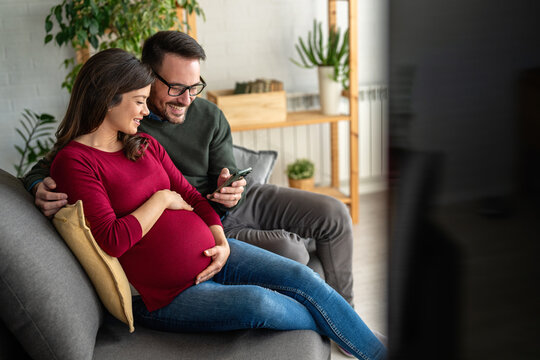 Happy young pregnant couple using virtual mobile service, online app on smart phone,