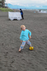 Little blond kid play football and have fun on black sand beach in Kobuleti, Georgia