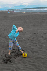 Little blond kid play football and have fun on black sand beach in Kobuleti, Georgia