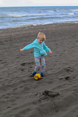 Little blond kid play football and have fun on black sand beach in Kobuleti, Georgia