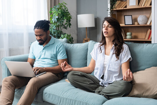 Couple balancing remote life at home, one partner stressed with laptop deadlines while the other meditates to stay centered, illustrating mindful relationship care, mental health, focus and resilience - Powered by Adobe