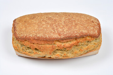 A fresh, oblong loaf of rustic whole grain bread with a textured brown crust is photographed on a plain white background