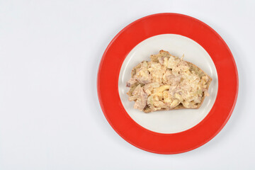 A top-down shot of an open-faced sandwich topped with creamy chicken salad on a whole-grain bread slice, served on a white plate with a striking red rim