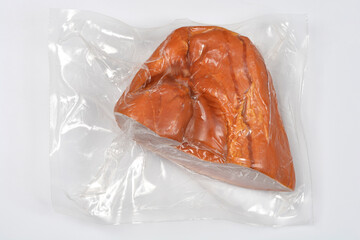 A piece of smoked pork meat, dark orange-brown in color, is tightly vacuum-sealed in clear plastic...
