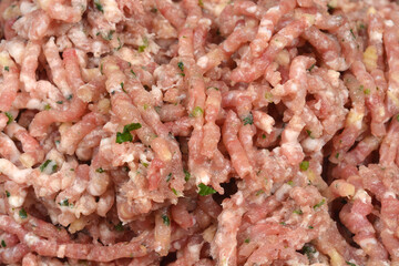 A close-up background image of freshly ground raw pork, which has been mixed with green herbs and spices, showing the coarse, extruded texture