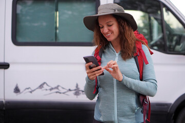 woman wearing a hat, hiking clothes, and a backpack, starting the route on her mobile app