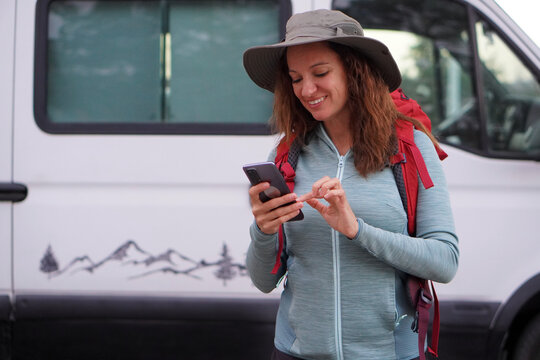 woman wearing a hat, hiking clothes, and a backpack, starting the route on her mobile app