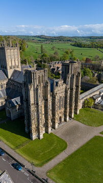 Aerial view of the majestic Wells Cathedral rising from the Cathedral Green, its stone facade contrasting with the lush green fields beyond, Wells, England, United Kingdom.