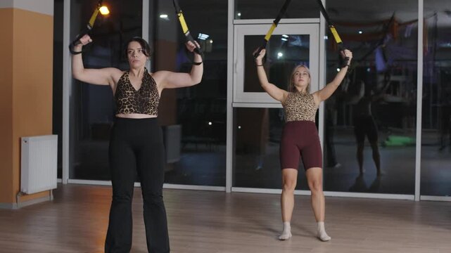 Women performing suspension training exercises in gym with slow motion focus on stretching and strength building