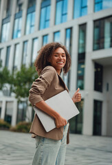 young black woman holding laptop confidently, walking toward office entrance, bright smile,...