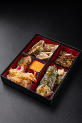 Bento box with gyoza, sushi, salmon and tempura on dark background isolated for menu