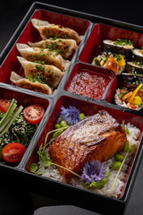 Bento box with gyoza, sushi, salmon and tempura on dark background isolated for menu