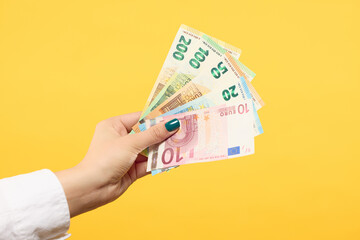 Woman hand holding euros banknotes isolated on yellow background. Finance concept.