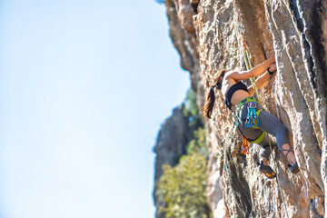 Woman rock climbing. Strong girl climbing a rock. Extreme hobby. Overcoming a difficult rock climbing route. Overcoming fear of heights. Efforts in rock climbing.