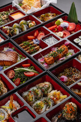 Huge bento box with Japanese cuisine dishes - sushi, sashimi, gyoza, tempura and more on a dark background isolated