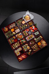 Huge bento box with Japanese cuisine dishes - sushi, sashimi, gyoza, tempura and more on a dark background isolated
