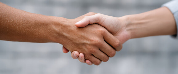 Close-up of two diverse hands shaking in agreement with blurred neutral background symbolizing partnership and cooperation